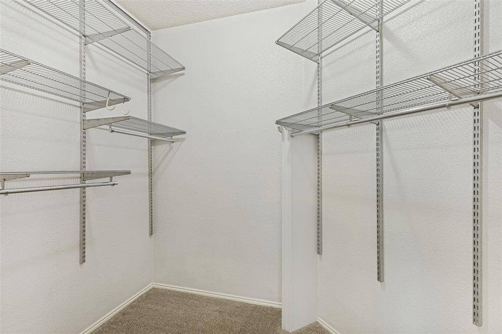 Storage space featuring white walls, neutral carpeting, and multi-level wire shelving with integrated hanging rods