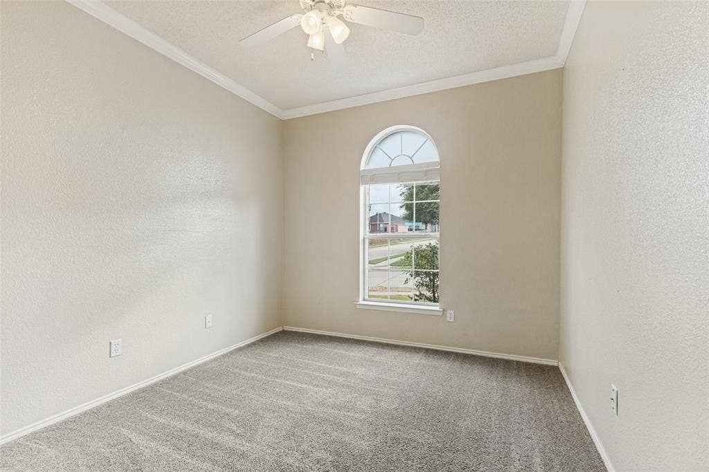 Room featuring neutral wall tones, arched window with muntin detailing, wall-to-wall carpeting, and a ceiling-mounted fan with integrated lighting