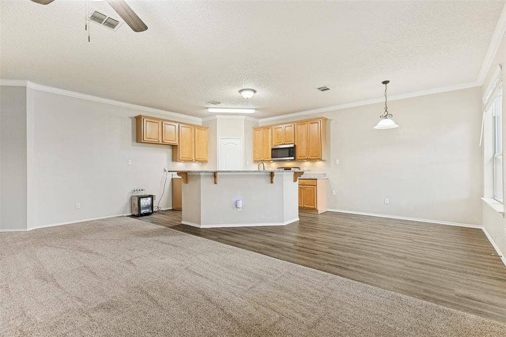 Kitchen featuring wood-finish cabinetry, stone-surface breakfast bar, wood-finish flooring, neutral carpeting, and overhead lighting fixtures