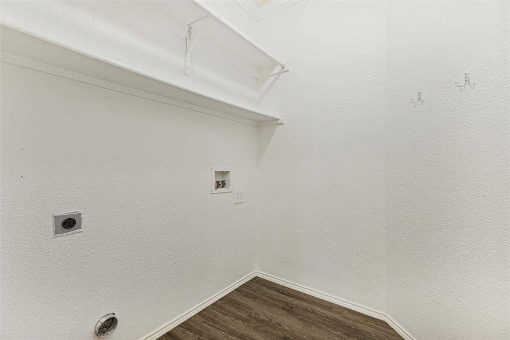 Utility area featuring wood-finish flooring, a wall-mounted shelving unit, and dedicated utility connections