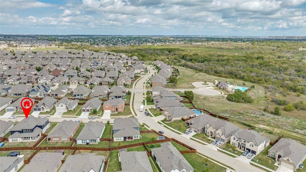 Aerial perspective of a multi-story residential structure featuring a dark shingled roof, neutral-toned exterior, and concrete driveway within a planned community setting