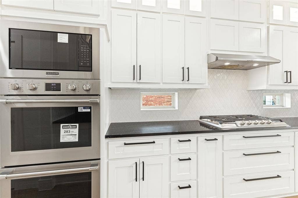 Kitchen featuring shaker-style white cabinetry, dark stone countertops, stainless steel wall-mounted oven and microwave, gas cooktop, and herringbone-patterned tile backsplash