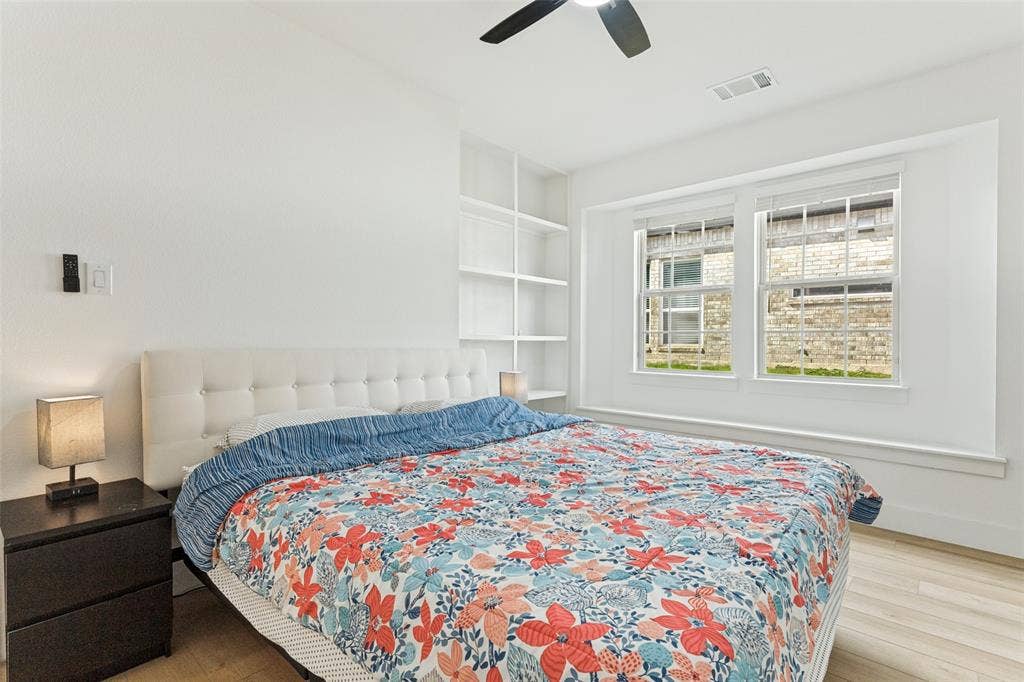 Room featuring wood-finish flooring, built-in white shelving, recessed window area, and a ceiling fan