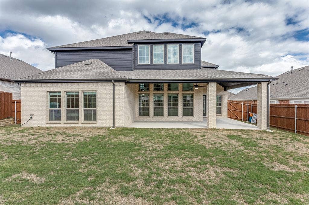 Two-story exterior featuring light brick masonry, dark horizontal lap siding, a covered concrete patio, and a shingle roof