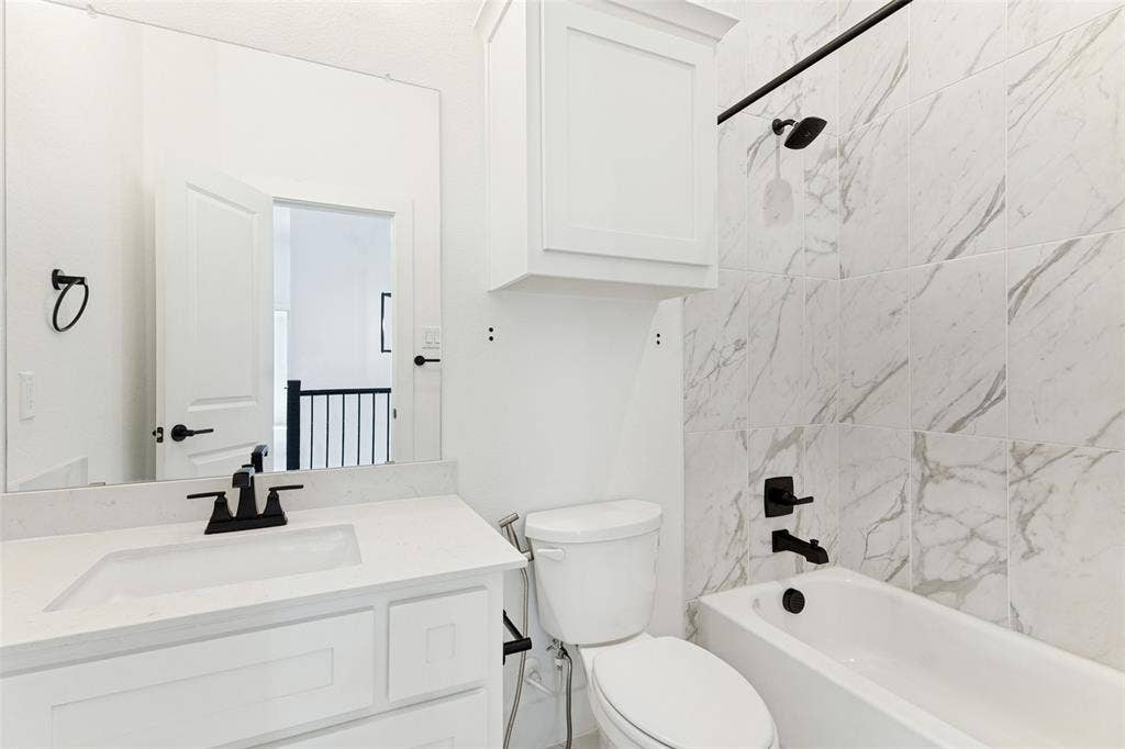Bathroom featuring a vanity with a white countertop and rectangular sink, matte black hardware, large-format tile shower surround, and white shaker-style cabinetry