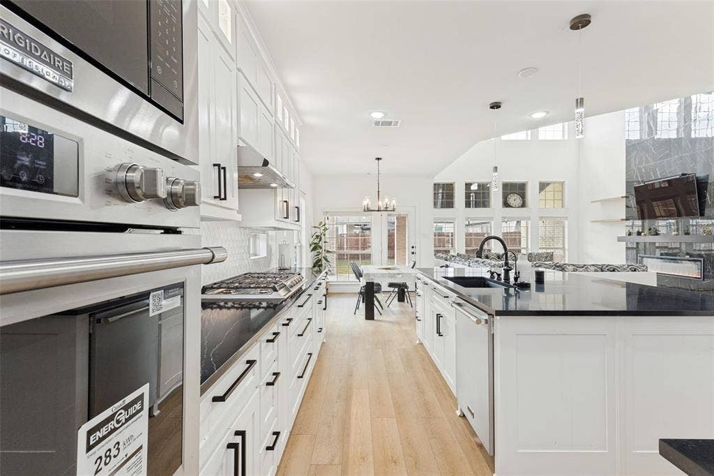 Kitchen featuring white shaker-style cabinetry, dark stone countertops, stainless steel appliances, wood-finish flooring, and a large center island with an undermount sink
