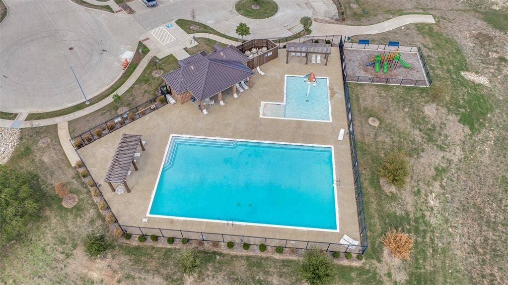 Community recreational facility featuring an expansive swimming pool, a shallow splash area, a covered pavilion, and a fenced playground
