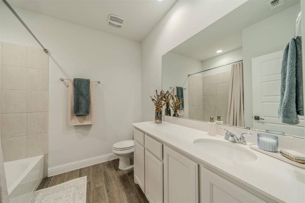 Full-width vanity with solid-surface countertop, integrated oval sink, chrome dual-handle faucet, large vanity mirror, and wood-finish flooring