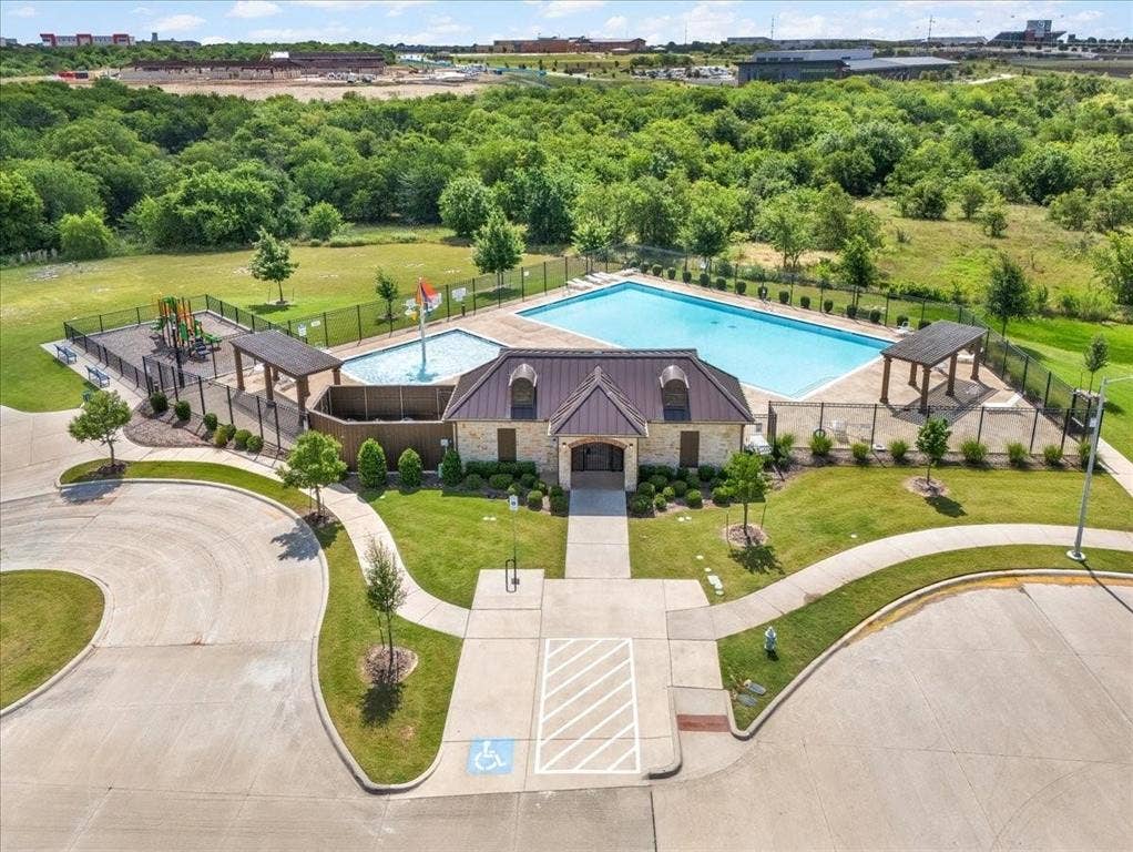 Community recreation area featuring a swimming pool, shallow splash pad with water feature, covered cabana structures, and a playground enclosure