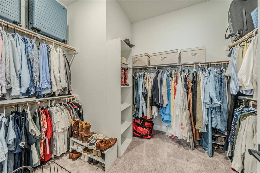 Walk-in closet featuring tiered shelving, built-in vertical storage tower, dual-level hanging rods, and neutral carpeting