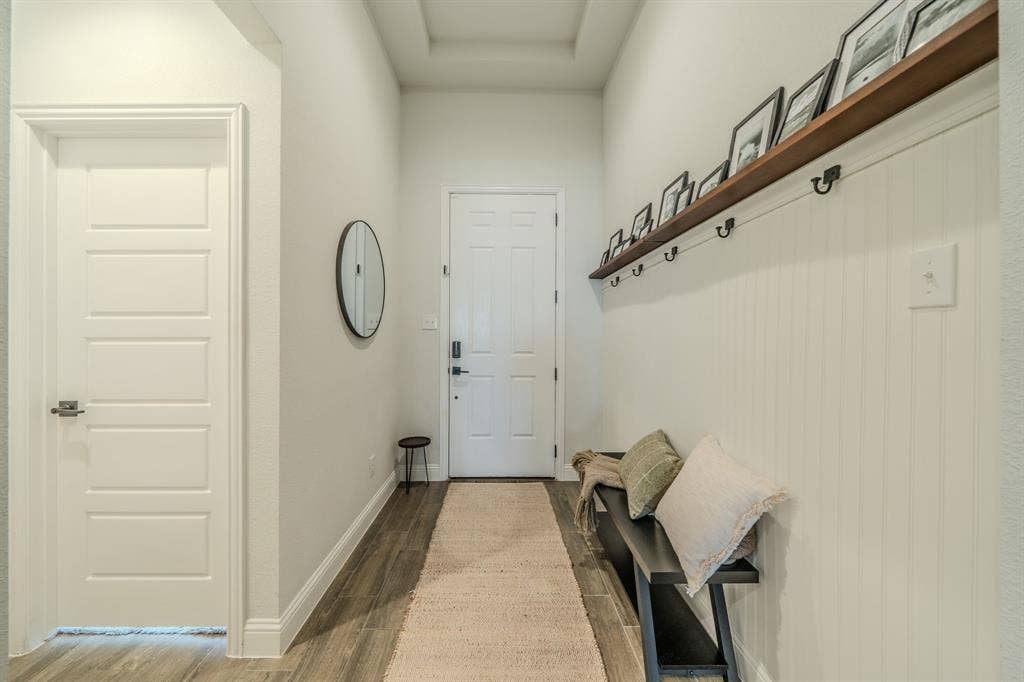 Entryway featuring wood-finish flooring, white beadboard wainscoting, a full-width wall-mounted display shelf with integrated hooks, and a tray ceiling