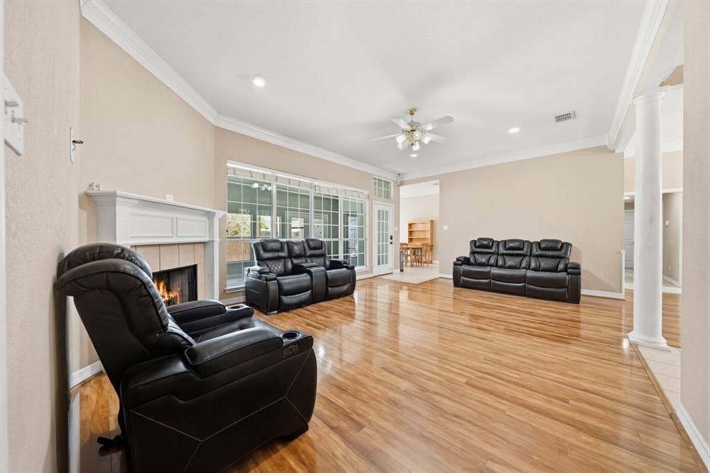 Living area featuring wood-finish flooring, white crown molding, a fireplace with a white mantel, multi-pane windows, and a decorative pillar