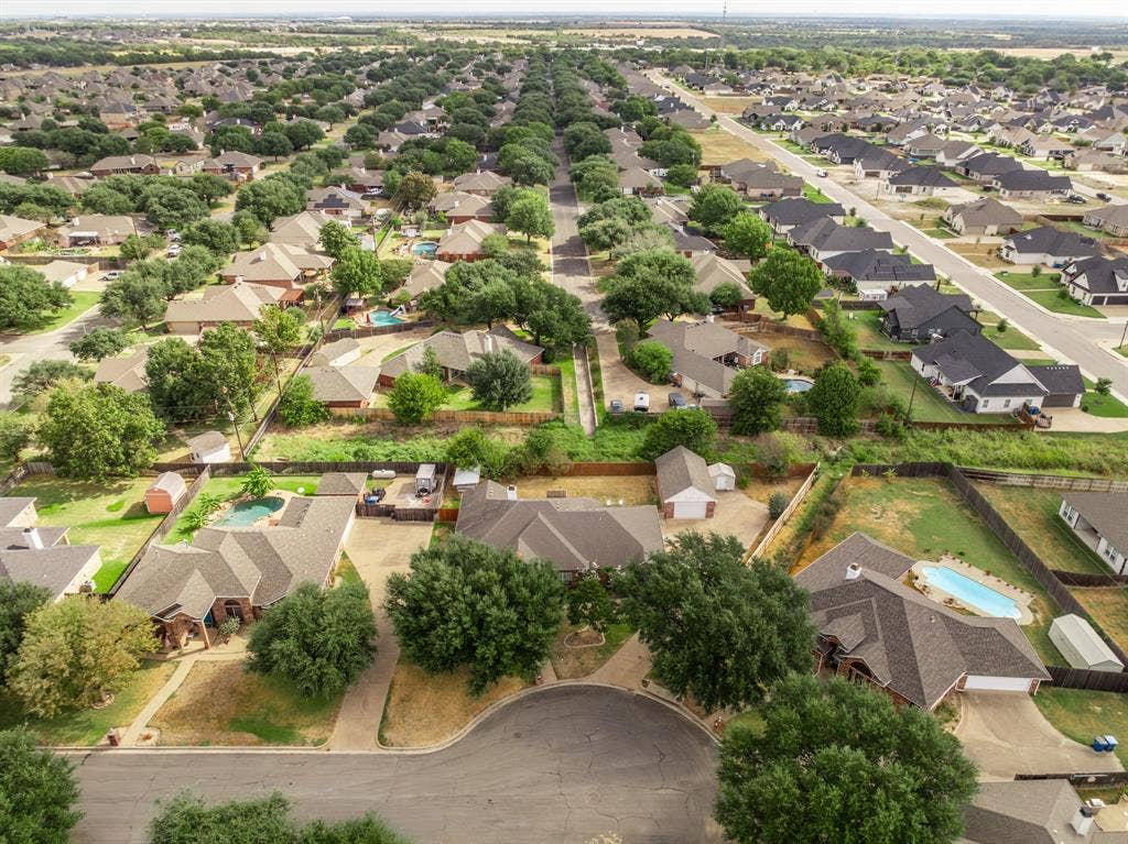 Aerial perspective of a suburban neighborhood featuring paved cul-de-sac streets, residential properties with shingled roofs, detached garages, private swimming pools, and mature trees