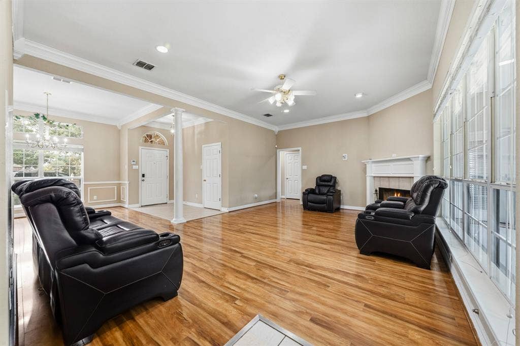 Living space featuring wood-finish flooring, a traditional fireplace with a white mantel, crown molding, a decorative column, and expansive grid-pane windows