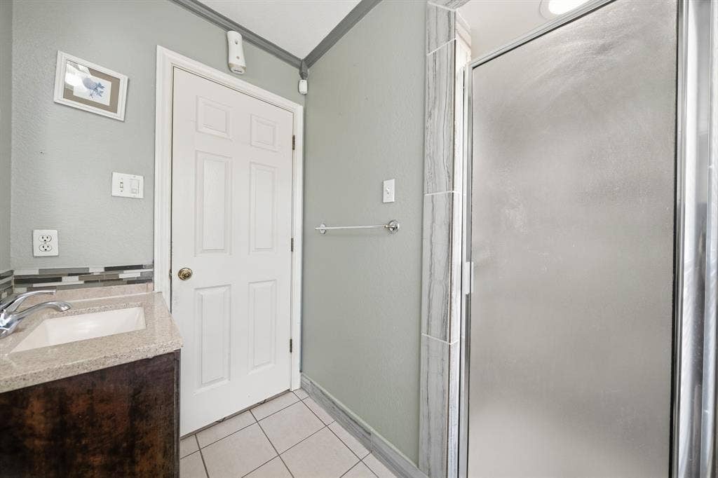 Bathroom featuring a vanity with a stone-finish countertop, tiled shower surround, frosted glass shower door, and ceramic tile flooring