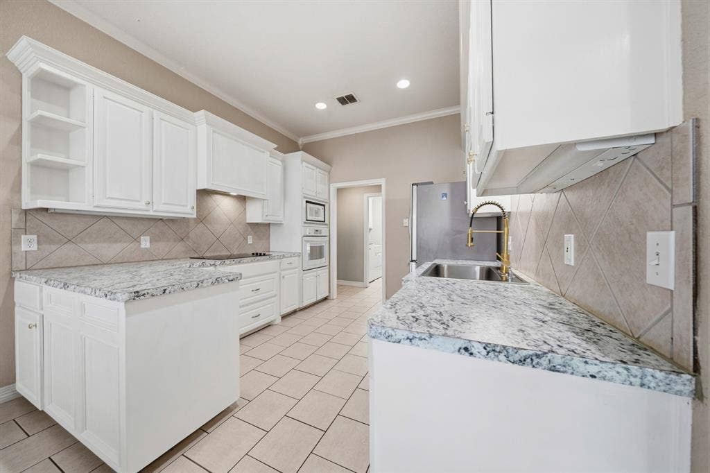 Kitchen featuring white cabinetry, stone-surface countertops, tile backsplash, tile flooring, and a gold-tone pull-down faucet