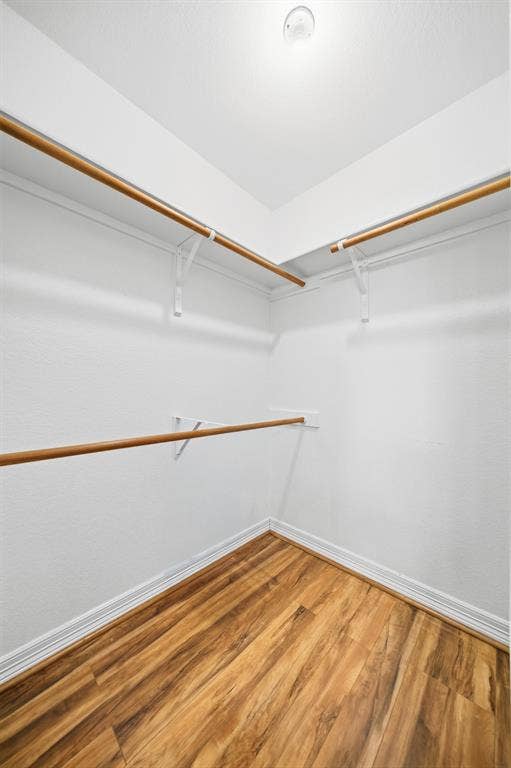 Walk-in storage featuring wood-finish flooring and tiered metal shelving rods