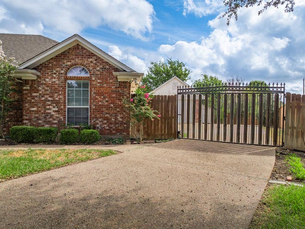 Brick exterior featuring a gabled roofline, an arched window, a concrete driveway, and a gated perimeter fence