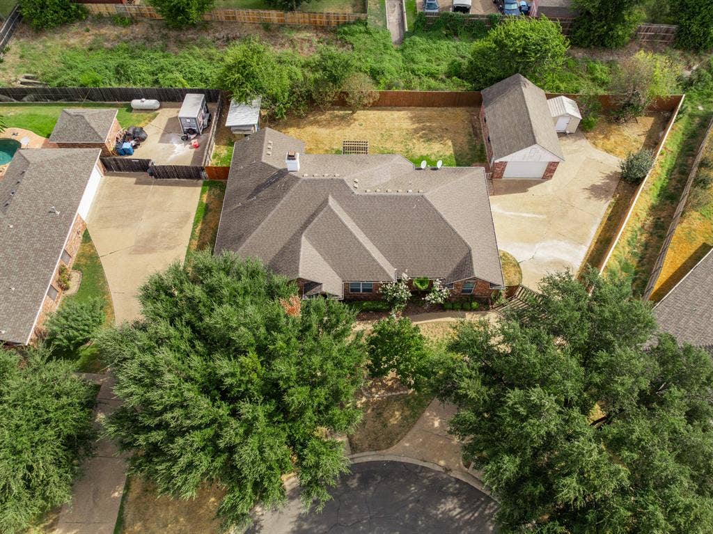 Aerial view featuring a multi-gabled roofline, brick exterior, detached garage, expansive concrete driveway, and fenced perimeter