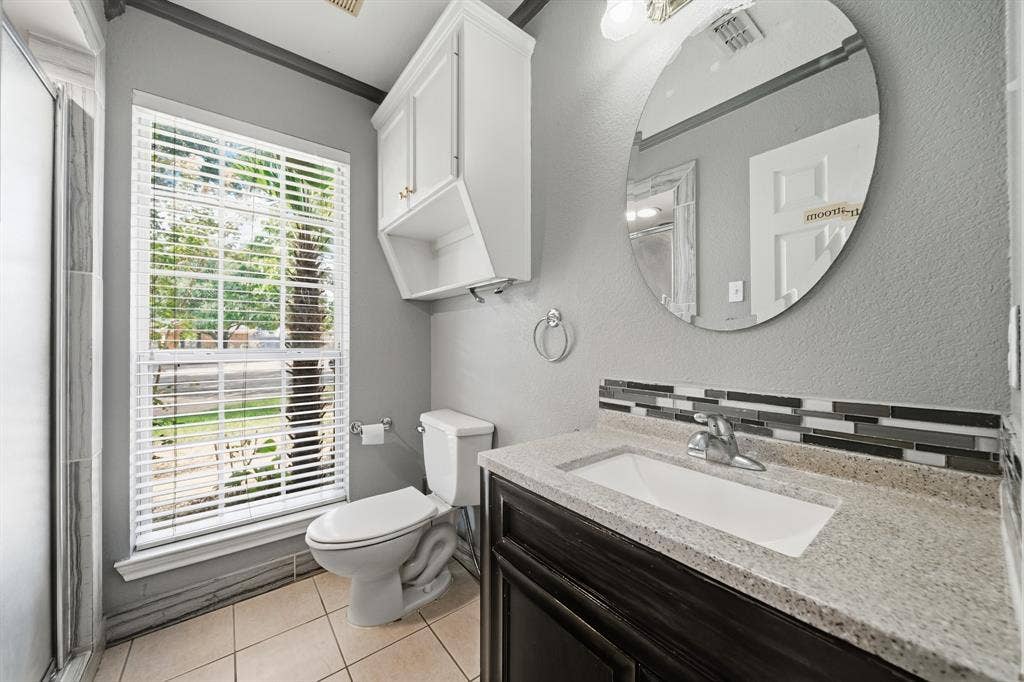 Bathroom featuring a dark wood-finish vanity, light-toned composite countertop, rectangular undermount sink, multi-tonal linear tile backsplash, and an oval wall-mounted mirror