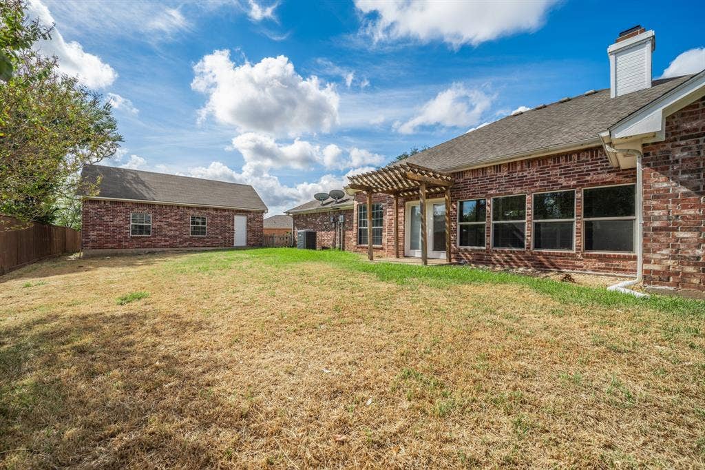 Brick exterior featuring a wooden pergola, detached auxiliary structure, and wood-panel fencing