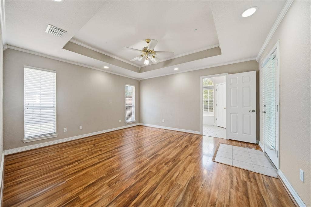 Tray ceiling featuring recessed lighting and a central ceiling fan, expansive wood-finish flooring, and natural light provided by multiple windows