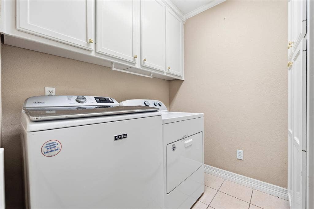 Laundry area featuring white shaker-style wall cabinets with brass-finish hardware, built-in floor-to-ceiling cabinetry, and neutral tile flooring