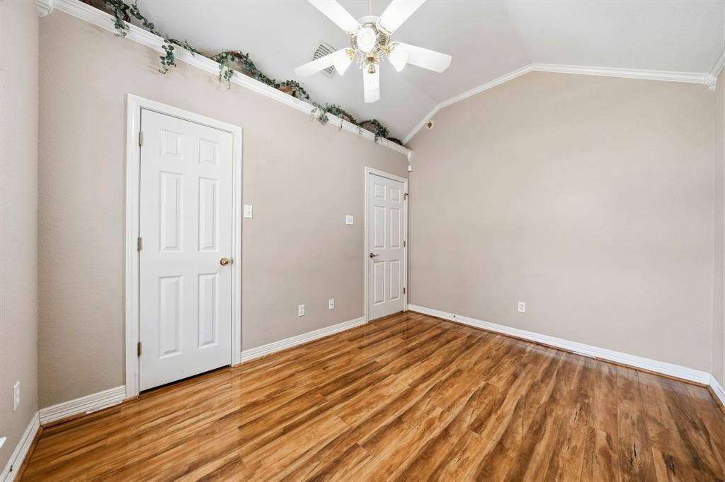 Vaulted ceiling featuring a central multi-blade ceiling fan and wood-finish flooring