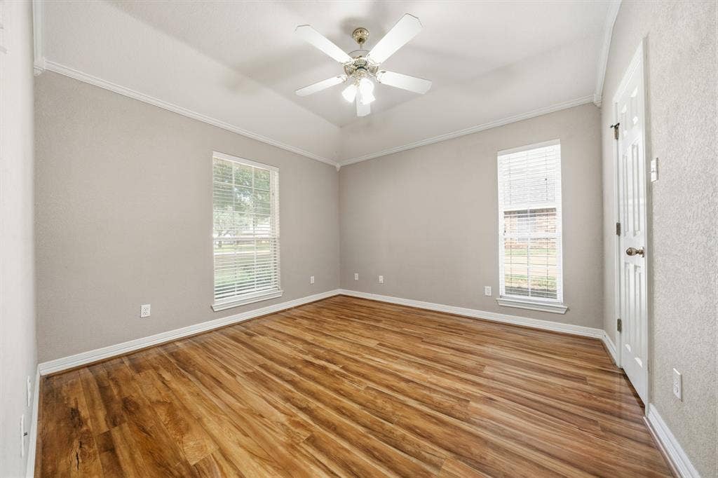 Room featuring wood-finish flooring, tray ceiling, multi-pane windows, and a central ceiling fan with integrated lighting