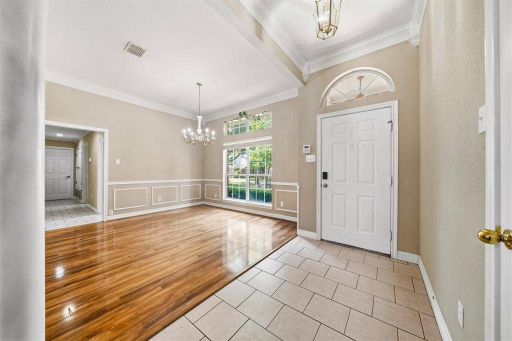 Entryway featuring large-format tile flooring, high ceilings with crown molding, wood-finish flooring, wainscoting, and a multi-pane front door with an arched transom window