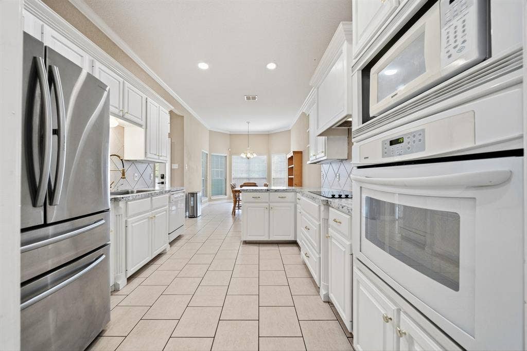 Kitchen featuring white shaker-style cabinetry, stainless steel refrigerator, built-in double oven, ceramic tile flooring, and stone-finish countertops