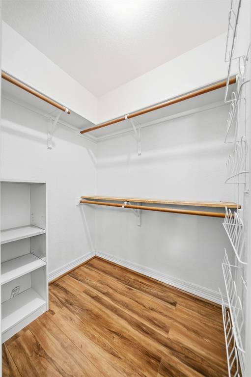 Walk-in closet featuring wood-finish flooring, multi-level clothing rods, built-in shelving, and white wire organizational racking
