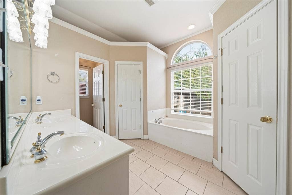 Dual-sink vanity with a solid-surface countertop, arched picture window, deep soaking tub, and tile flooring