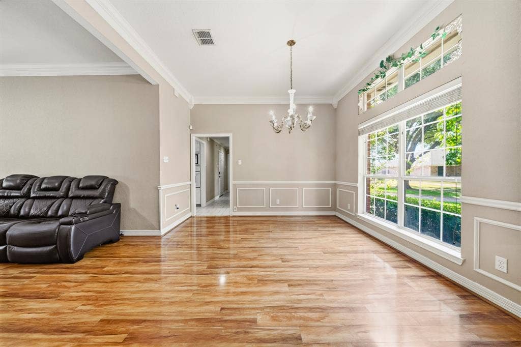 Wood-finish flooring, wainscoting, high ceilings with crown molding, multi-pane windows with a transom, and a central chandelier