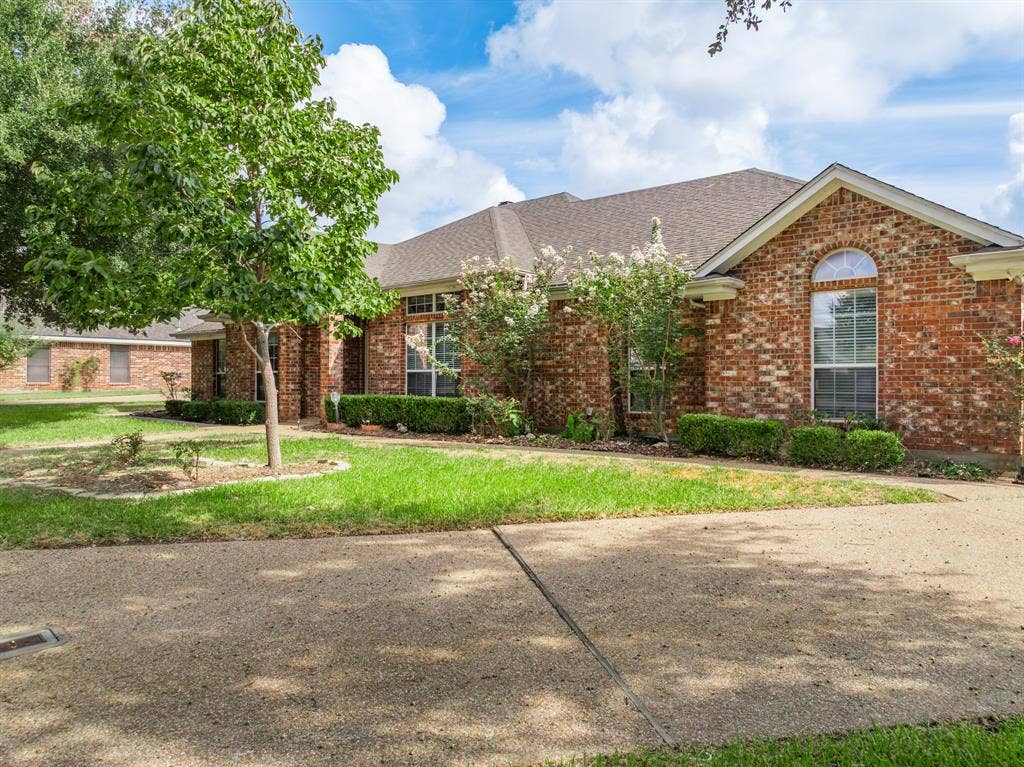 Single-story brick exterior featuring a multi-gabled roofline, an arched window, a textured concrete driveway, and mature landscaping