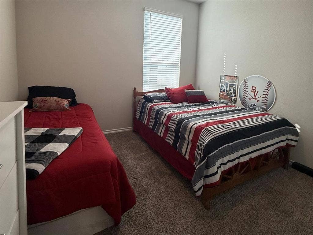 Neutral-toned bedroom featuring plush carpeting, textured wall finish, and a large window equipped with horizontal blinds