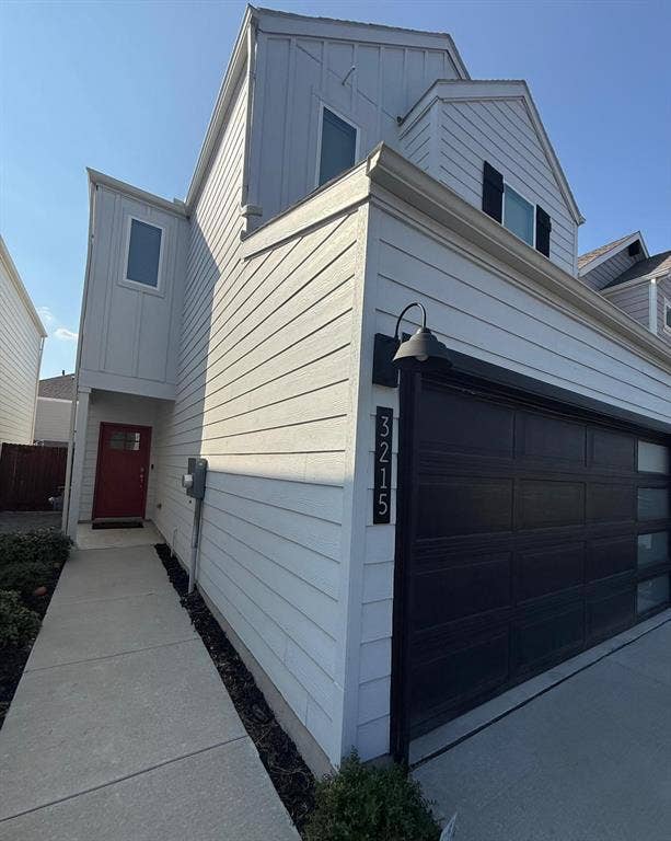 Multi-level exterior featuring horizontal siding, a red entry door, an attached two-car garage with a semi-opaque paneled door, and an exterior gooseneck light fixture