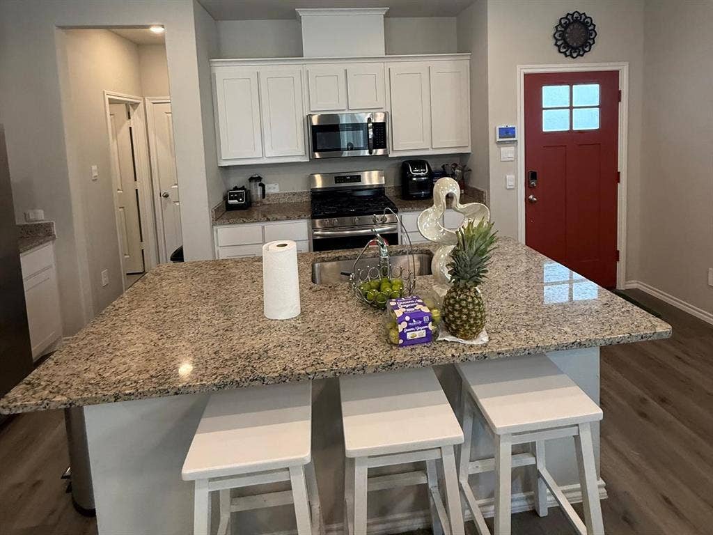 Kitchen featuring a central island with stone countertop, white shaker-style cabinetry, stainless steel appliances, and wood-finish flooring