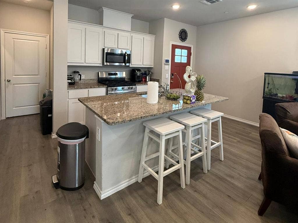 Kitchen featuring white cabinetry, stone-surface countertops, center island, stainless steel appliances, and wood-finish flooring