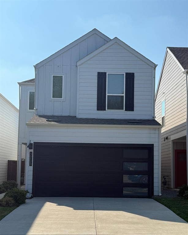 Two-story residence featuring light-colored horizontal and vertical siding, a decorative shuttered window, and a modern garage door with integrated glass panels