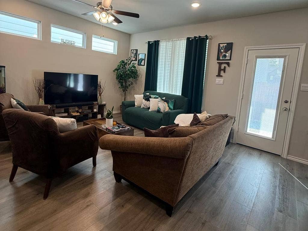 Living area featuring wood-finish flooring, high ceilings with a recessed lighting fixture, a ceiling fan, transom windows, and a glass-paneled exterior door
