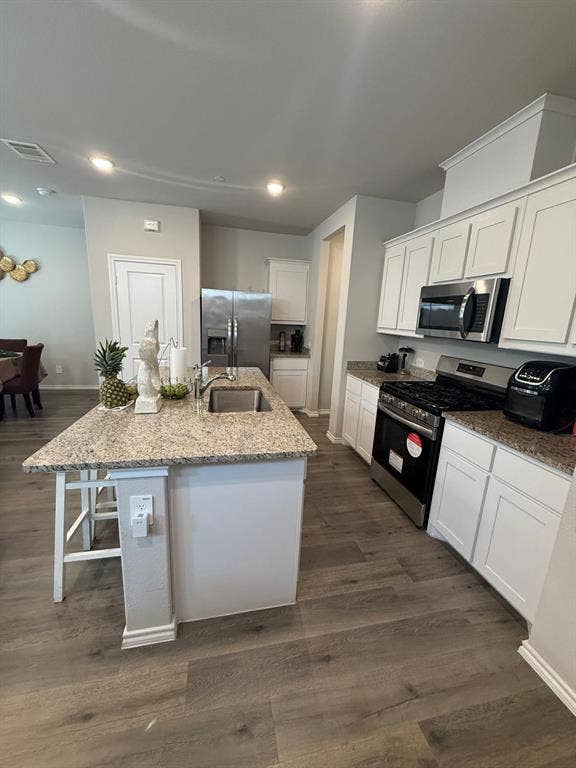Kitchen featuring a central island with a stone-surface countertop, white cabinetry, stainless steel appliances, recessed lighting, and wood-finish flooring