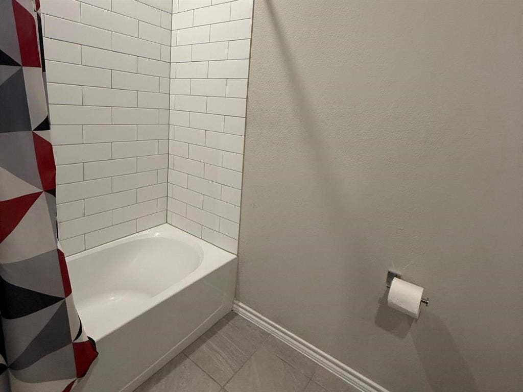 Bathtub enclosure featuring white subway tile surround and neutral-toned floor tile