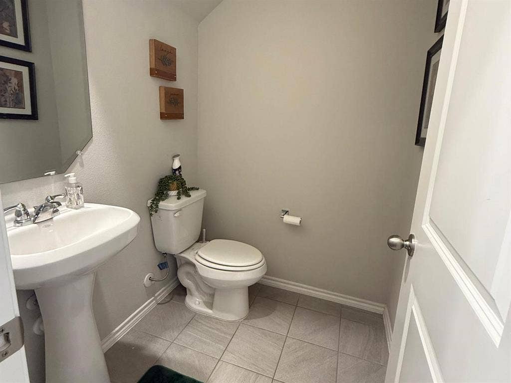 Powder room featuring a pedestal sink, dual-handle chrome faucet, wall-mounted mirror, and tile flooring