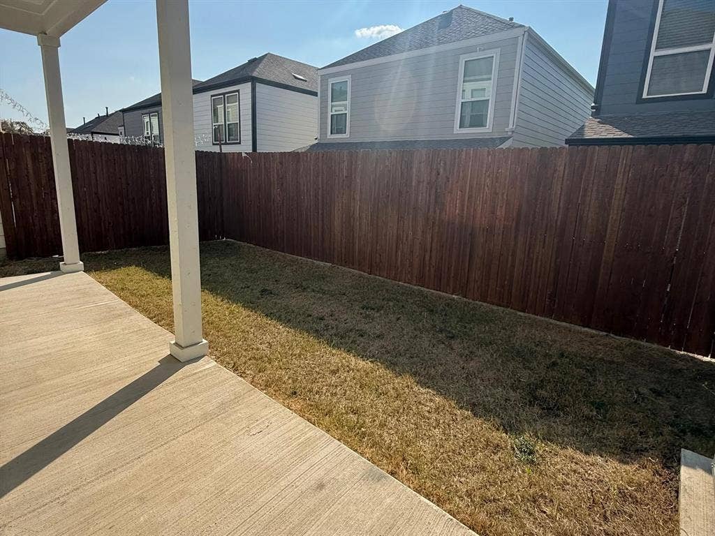 Covered concrete patio with square support columns, enclosed by a full-height wood privacy fence