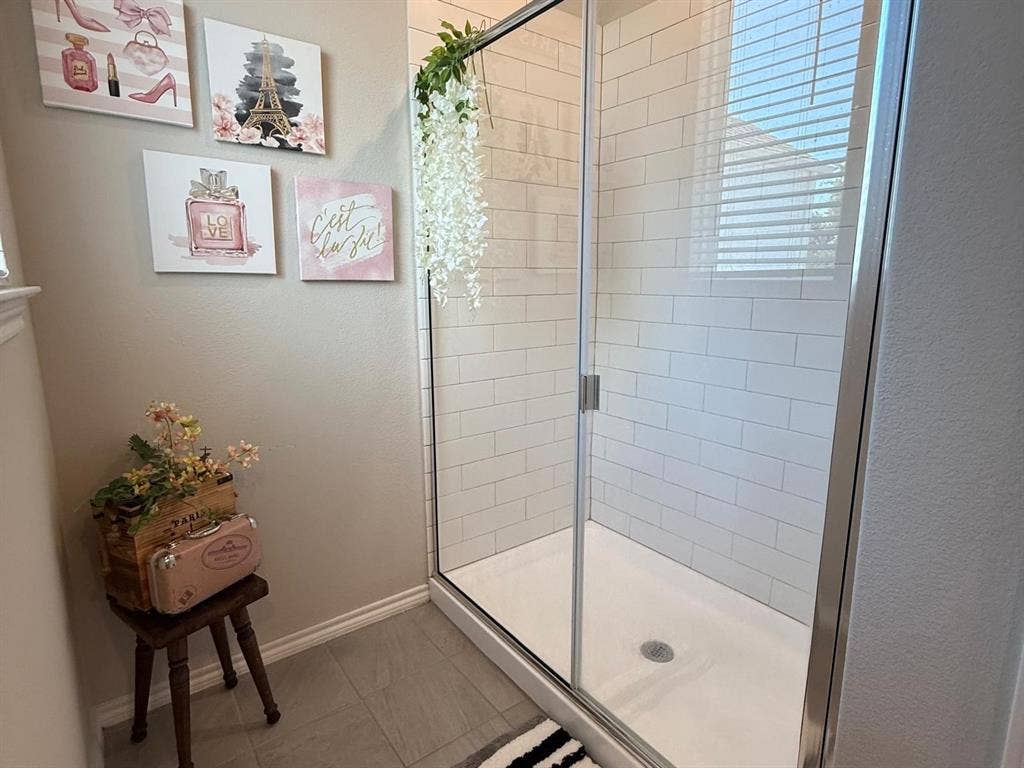 Walk-in shower featuring white subway-style wall tile, a metal-framed glass enclosure, and a built-in shower pan, complemented by neutral tile flooring