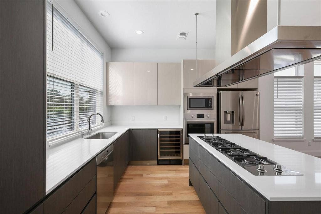4904 Lexington Court, Dallas, TX 75206 Kitchen featuring flat-panel cabinetry, quartz countertops, wood-finish flooring, a stainless steel gas cooktop set into a central island, and a built-in wine refrigerator