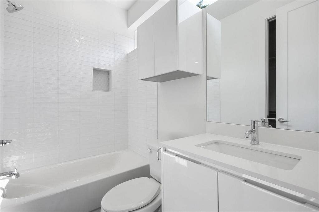 4904 Lexington Court, Dallas, TX 75206 Bathroom featuring a white gloss vanity with integrated sink, stone-finish countertop, white tile tub surround with built-in recessed niche, and wall-mounted storage cabinetry