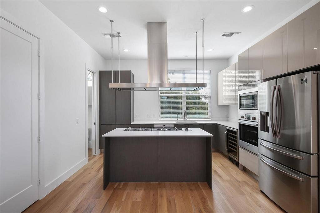 4904 Lexington Court, Dallas, TX 75206 Contemporary kitchen featuring wood-finish flooring, a central island with a gas cooktop, a stainless steel suspended range hood, custom cabinetry with high-gloss finishes, and a built-in stainless steel double wall oven