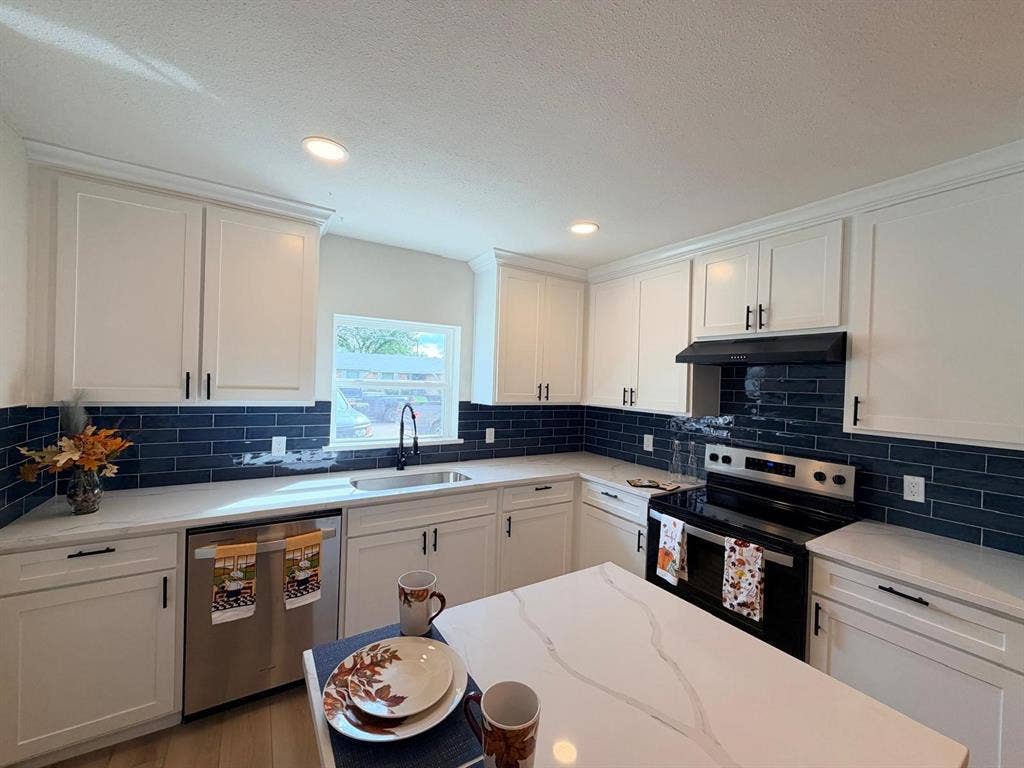 Kitchen featuring white cabinetry with matte black hardware, stone-finish countertops, dark-toned subway tile backsplash, and stainless steel appliances